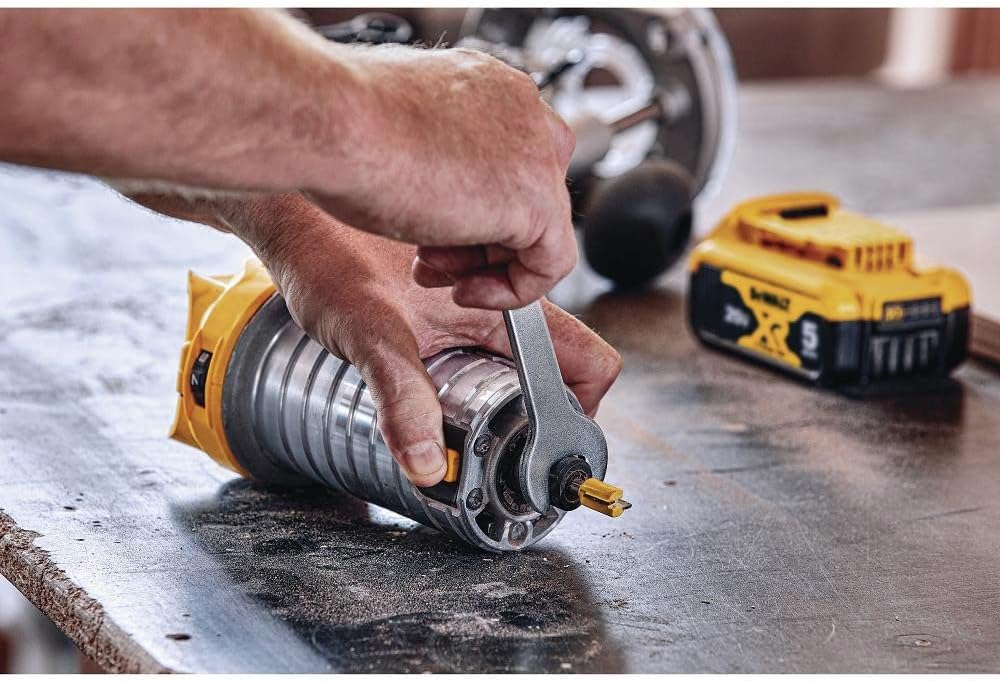 Hands using a wrench on the spindle lock to change a router bit, with a 20V MAX battery beside it