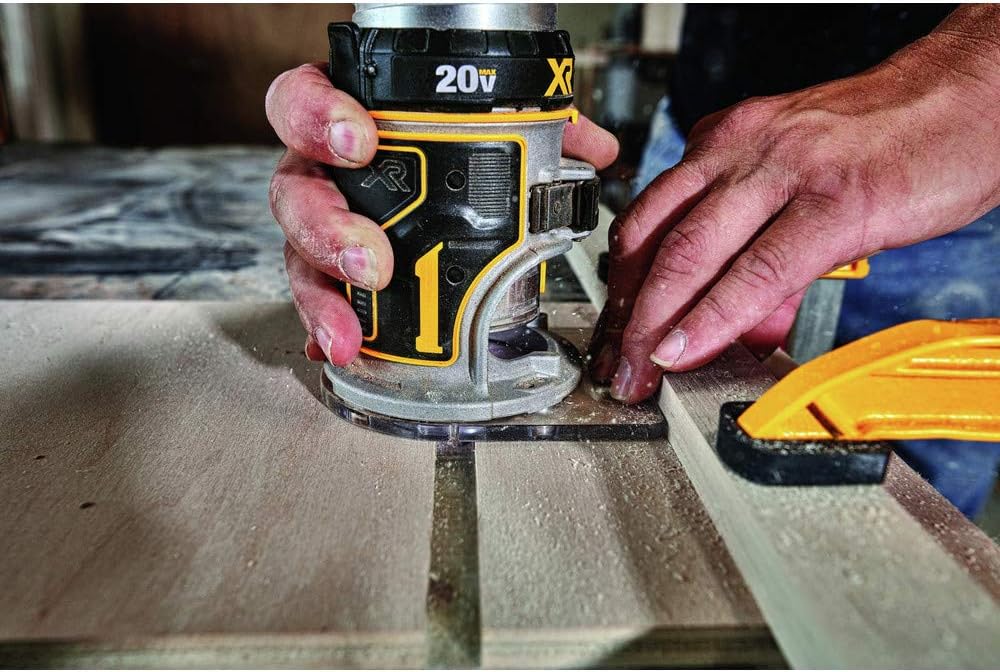 Hands guiding the DeWalt 20V MAX XR router along a board edge, cutting a groove with sawdust flying