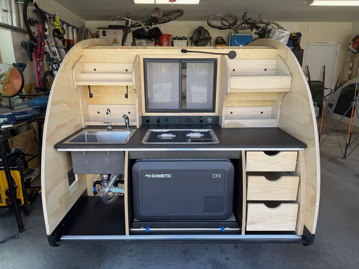 Wide view of the finished teardrop galley showing the sink, cooktop, drawers, and the Dometic CFX3 fridge in the lower bay