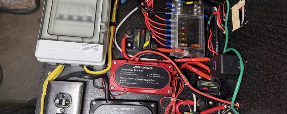A teardrop camper's power compartment fully wired, showing the AC breaker box, blade fuse block, and bus bars