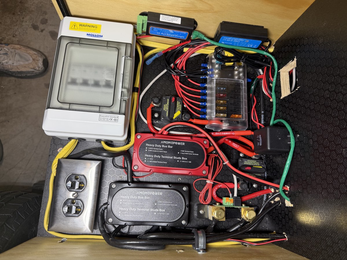 A teardrop camper's power compartment fully wired, showing the AC breaker box, blade fuse block, and bus bars