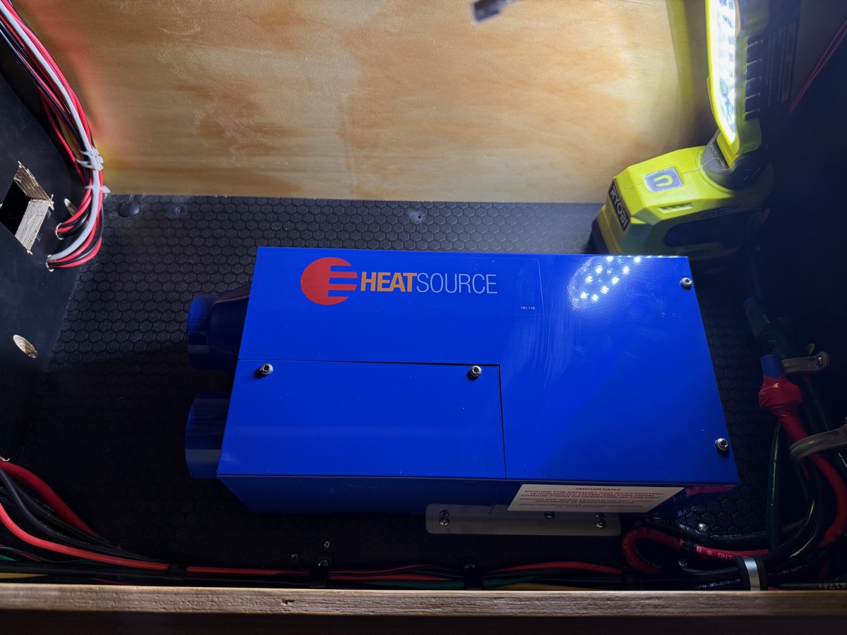 Blue Propex HeatSource propane furnace mounted inside a teardrop camper's compartment with red and black 12V power leads and ducting