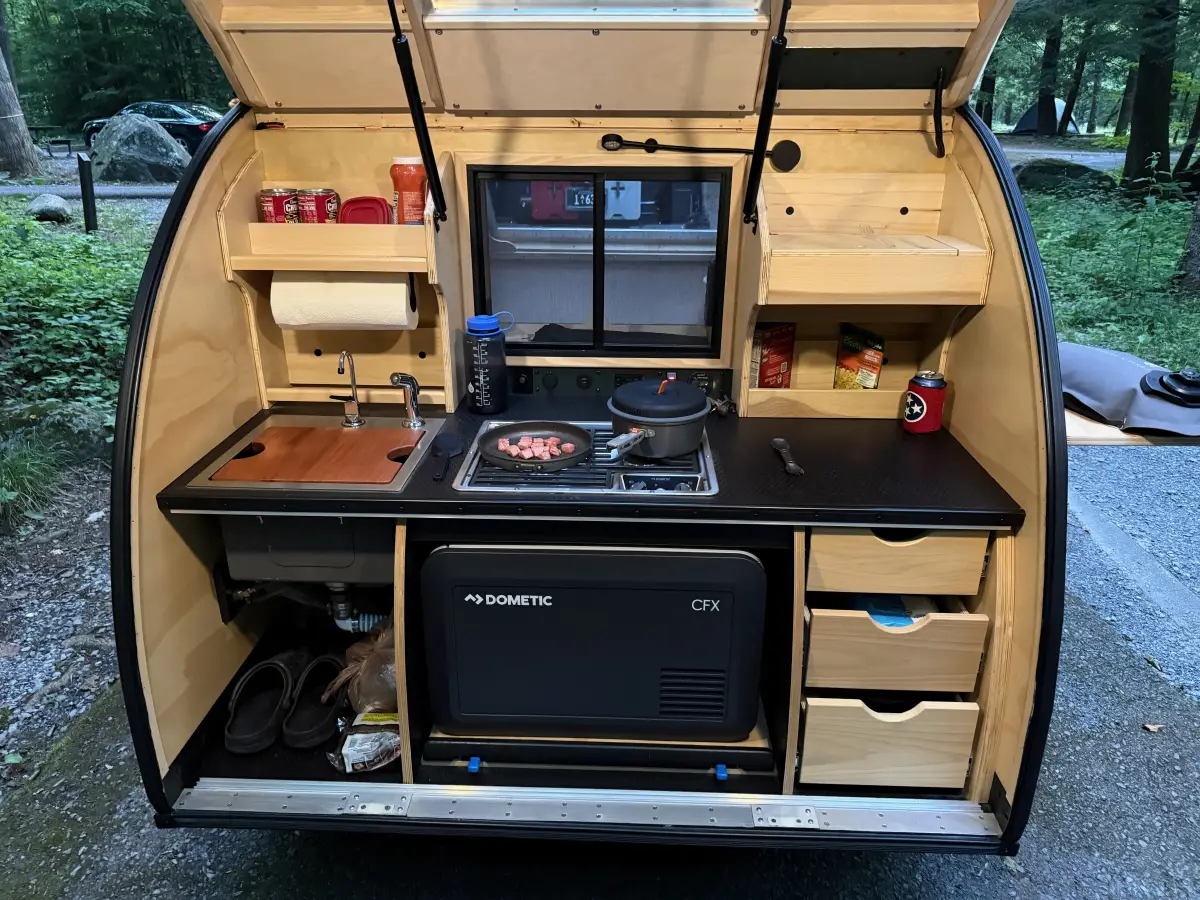 Dinner cooking in the rear galley of a teardrop camper with a dual burner propane stove and sink
