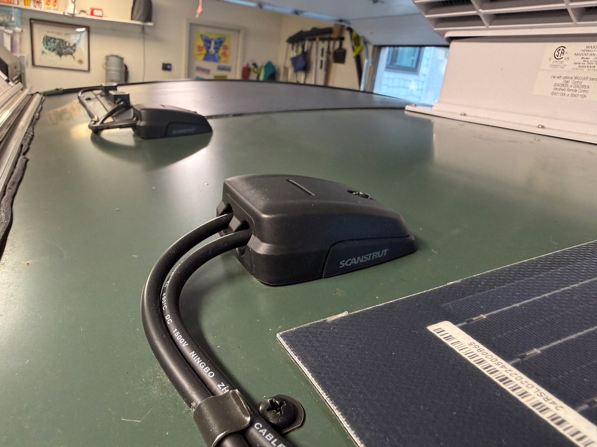A black Scanstrut two-entry cable gland on a teardrop roof with both solar leads entering it, the panel corner beside it