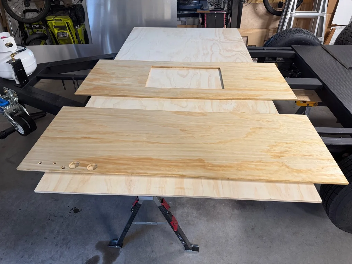 Raw plywood galley panels stacked and staged on a sawhorse in the garage before a coat of polyurethane