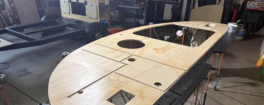 A large curved plywood teardrop side wall panel on sawhorses, waiting on a coat of polyurethane