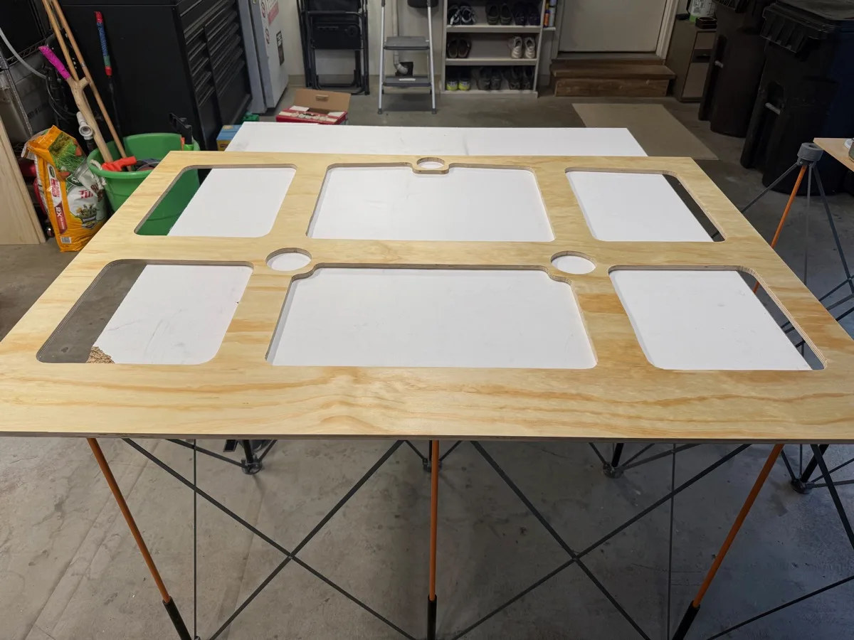 Plywood cabinet door blanks with cutouts laid out flat on a folding table in the shop, ready for finish