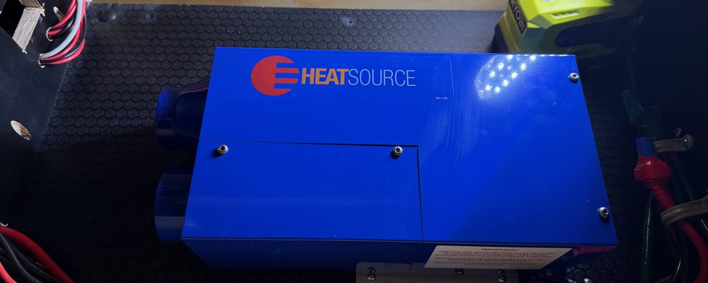 A blue Propex HeatSource propane furnace mounted on a rubber-matted floor inside a teardrop camper's utility bay