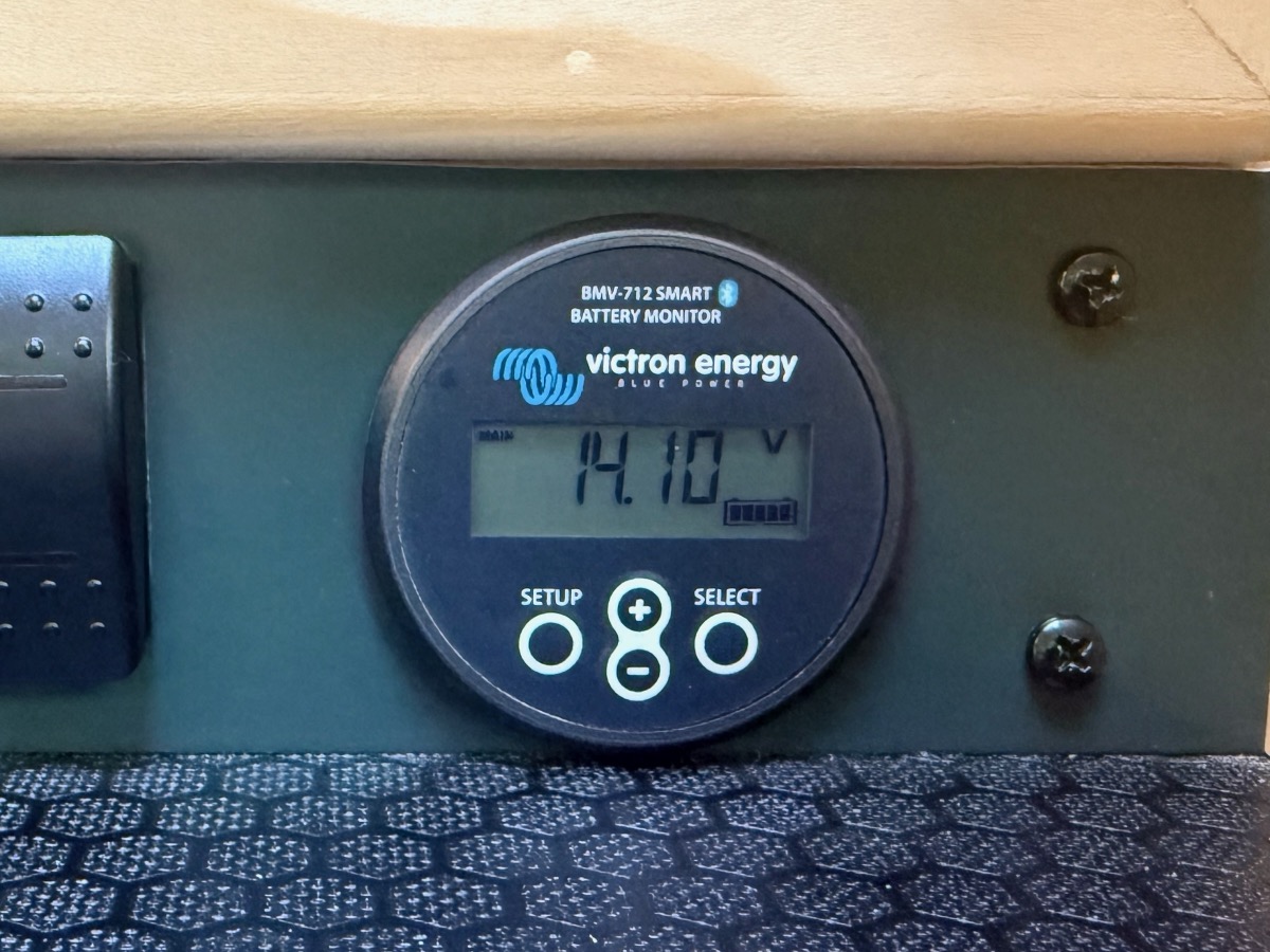 A Victron BMV-712 Smart battery monitor mounted in a teardrop camper galley panel, reading 14.10 volts