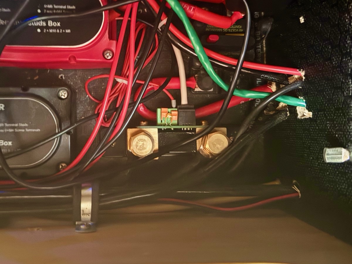 A battery monitor shunt with brass terminals wired into a teardrop camper's power bay alongside heavy-duty bus bars