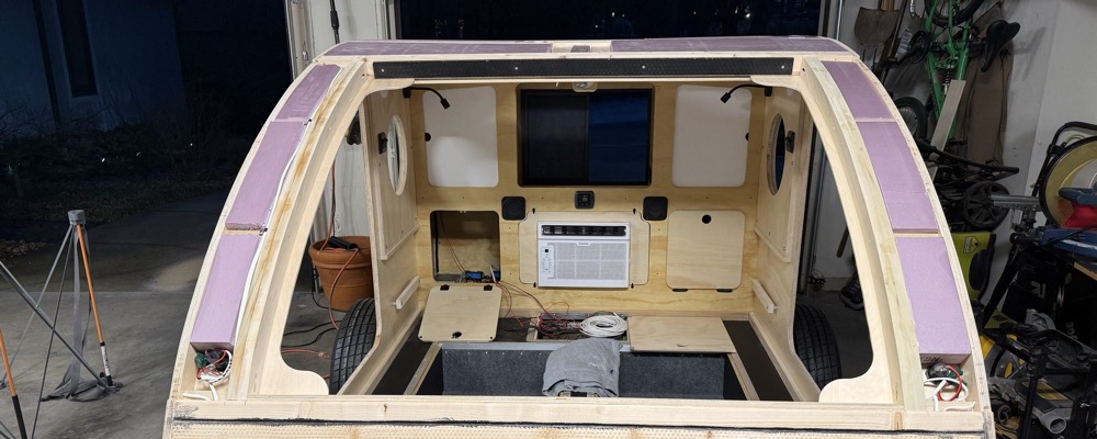 Rigid foam board fitted between the curved roof spars of a teardrop camper before the roof skin is installed