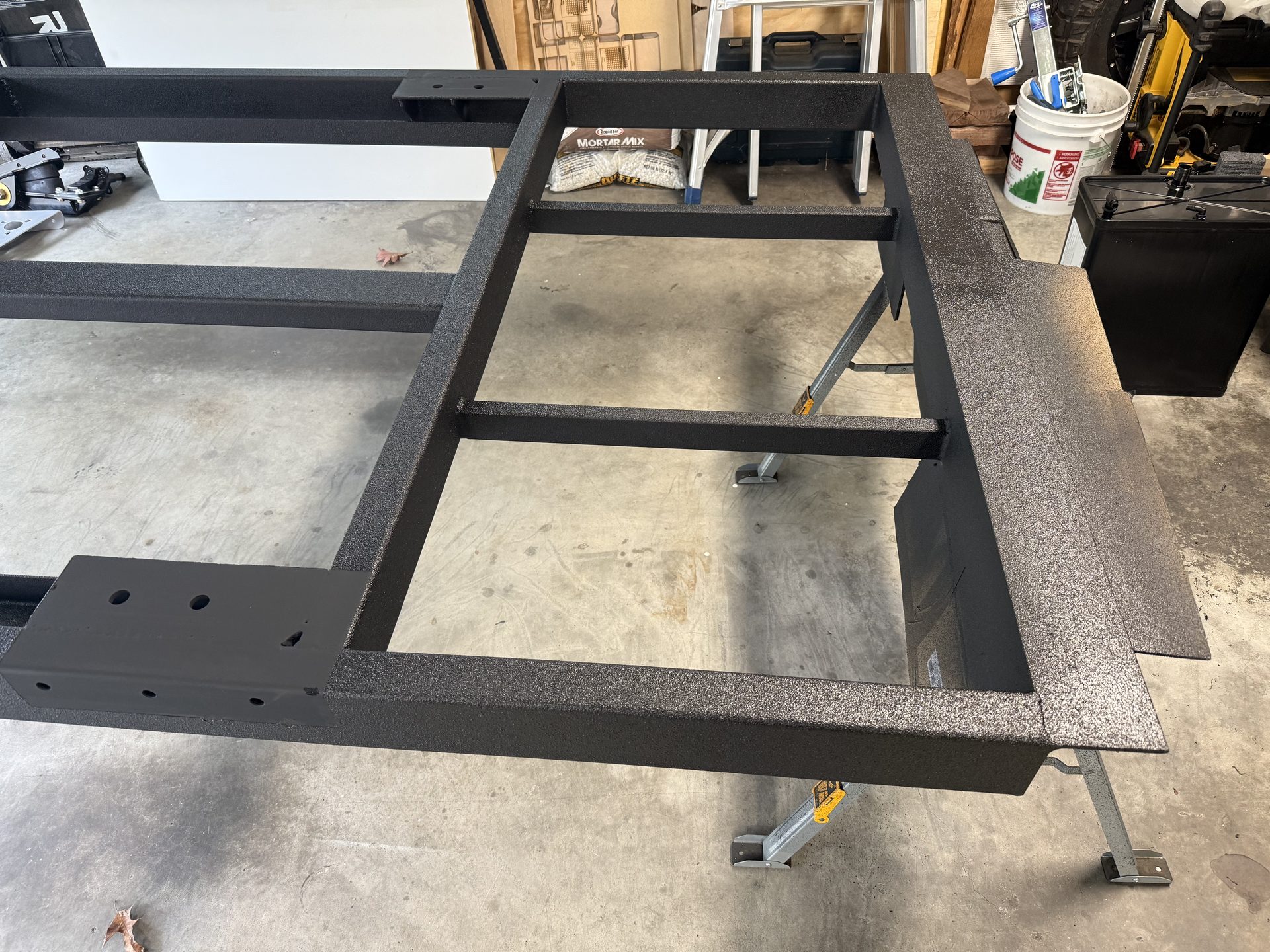 A painted steel teardrop trailer frame with open bays before the floor deck is installed
